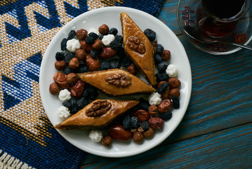 Azerbaijan national pastry pakhlava with sweet snack and glass of traditional black tea on wooden table with green semeni wheat grass background , Novruz tray spring celebration