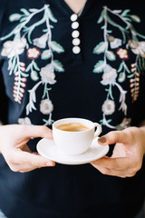 Very nice young woman holding a small cup of fresh espresso coffee in a white cup with a saucer, cropped photo