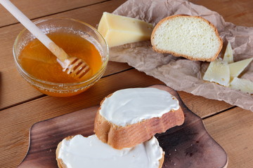 Hard cheese on a wooden board, food on parchment paper, sandwiches with soft cheese, honey in glass dishes, copy space, cheese pattern, wood background, wooden cutlery, simple food