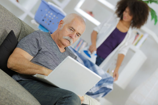 senior man with laptop and home help ironing