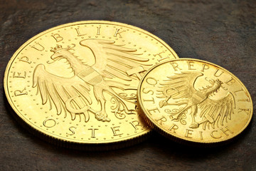 Austrian 25 and 100 Schilling gold coins on rustic wooden background