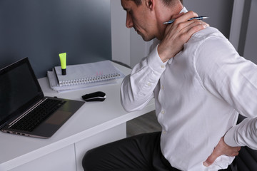 Business man suffering from back and neck pain in an office. Incorrect sitting posture problems,...