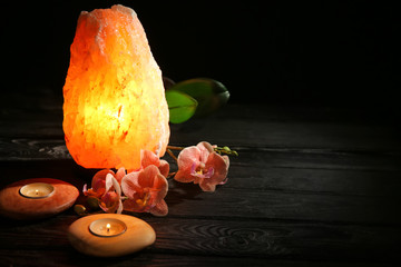 Himalayan salt lamp, candles and flowers on table against dark background