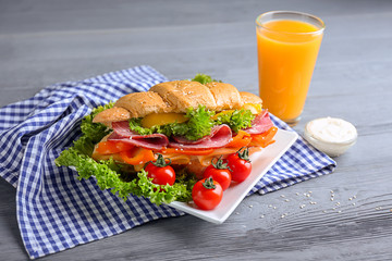 Plate with tasty croissant sandwich and glass of juice on table