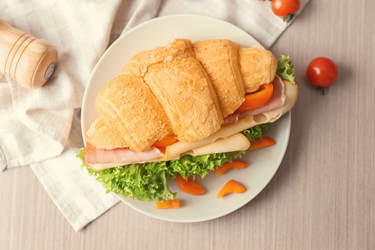 Plate with tasty croissant sandwich on table
