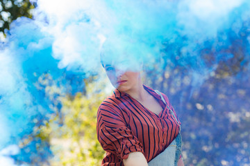 Young mixed race woman dressed in grungy hipster style outdoors poses with colored smoke bombs