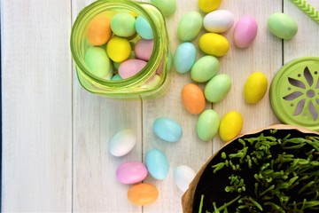 Fototapeta na wymiar Green transparent glass jar with colored Easter eggs on the white wooden background