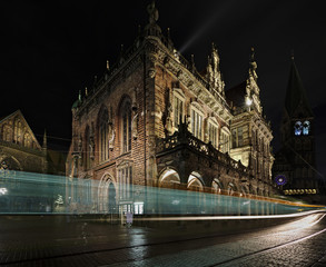 Fototapeta premium Historic city hall in Bremen, Germany at night with St Paul's Cathedral and the Church of our Lady in the background and tram passing by (long exposure)