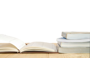 Pile of books with open book on wooden table.