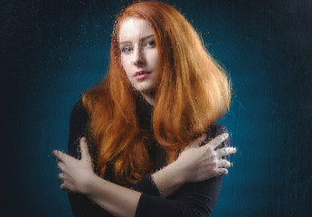 Beautiful, young red-haired girl behind a blind window