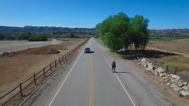 Aerial footage following a man riding an electric unicycle down a road in California.