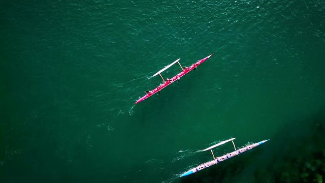 Beautiful aerial over a red outrigger canoe paddled on blue water.