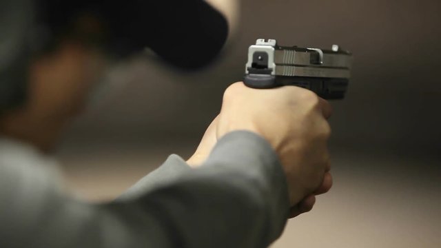 A man fires a hand gun at a target at an indoor shooting range.