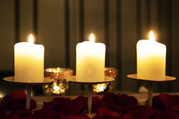 Blurred romantic evening background texture of three hot candles and rose petals.