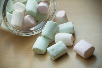 closeup of marshmallows falling from glass container on wooden table background