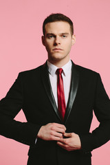 Handsome young man in black suit and tie on pink background