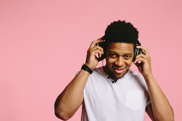 Fototapeta premium Portrait of a cool guy with headphones smiling and looking at camera, enjoying music, on pink background