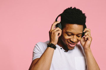 Portrait of a smiling guy in white shirt  listening to music and looking down, isolated on pink background