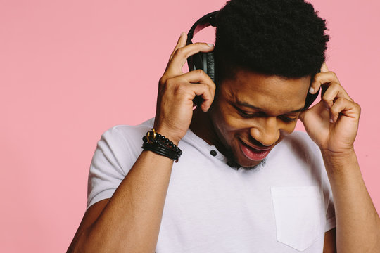 Portrait of a cool young guy listening to music with headphones on pink background