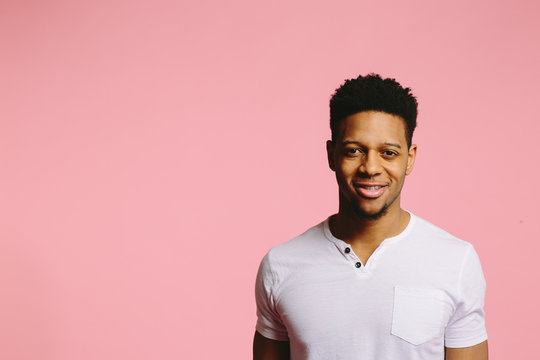 Portrait of an attractive African American guy in white shirt on pink background