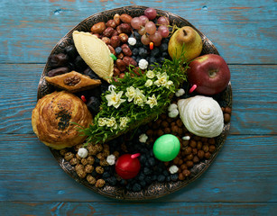 Novruz tray with Azerbaijan national pastry pakhlava,  shekerbura, gogal, badambura and dry snacks with green semeni wheat grass on rustic wooden table background