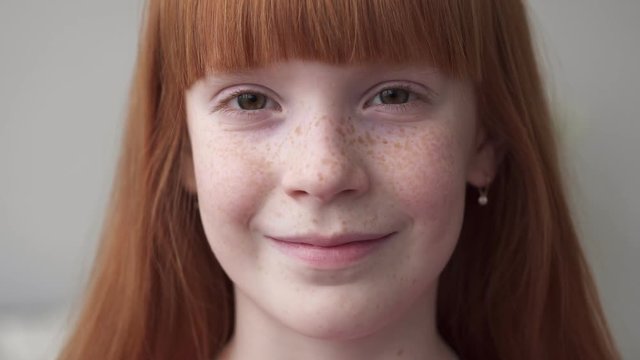Close-up of a face little ginger girl with freckles smiling