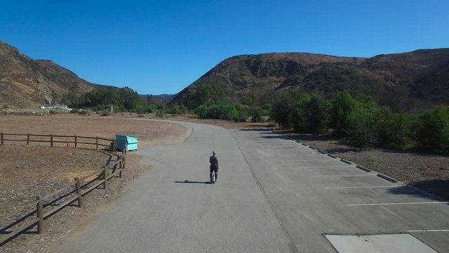 Aerial footage following a man riding an electric unicycle down a road in California.
