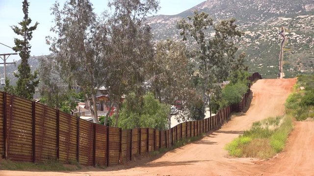 The U.S. border wall fence with the city of Tecate Mexico background.