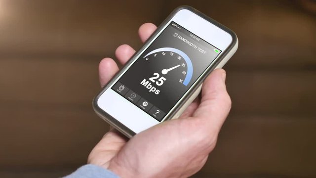 A man tests his home Internet bandwidth by running a speed test app on his smartphone. Result is 25 Mbps.  	