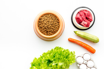 Dry pet food with natural ingredients. Raw meat, vegetables zucchini and carrot near eggs on white backgroud top view copy space