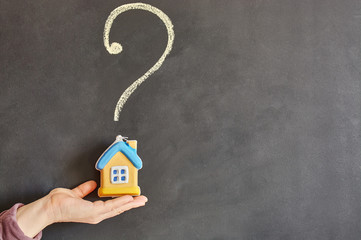 A female hand holds a toy house on the palm of a hand against the background of a question mark...