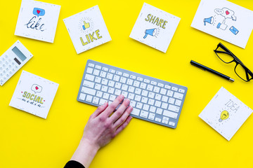 Social media promotion. Work desk with socail media icons. Yellow background top view. Hand is typing