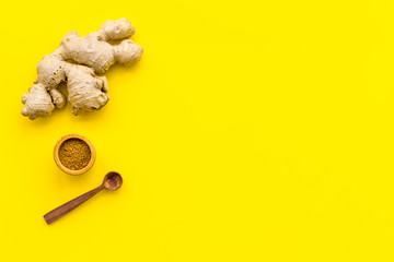 Seasoning. Ground ginger in small bowl near ginger root on yellow background top view copy space