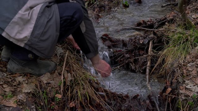 Man washes his hands in a forest creek - (4K)