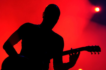 Silhouette of an unrecognizable man playing an electric guitar in a red background