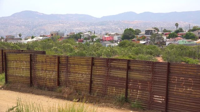 The U.S. border wall fence with the city of Tecate Mexico background.
