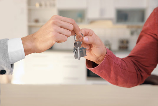 Real estate agent giving house key to young man indoors