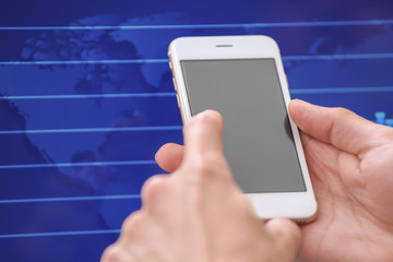 Man using smartphone near computer with stock chart data on screen. Forex concept