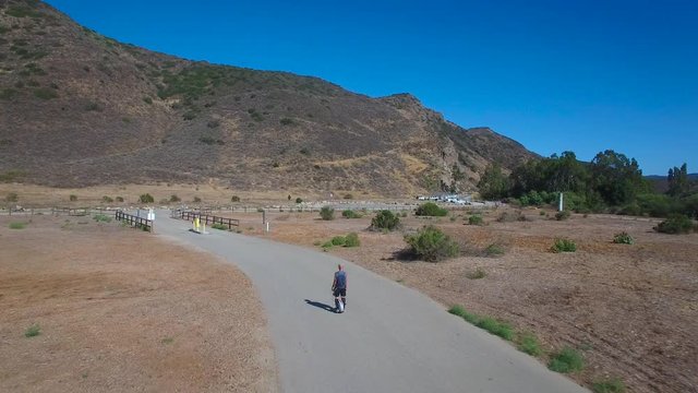 Aerial footage following a man riding an electric unicycle down a road in California.