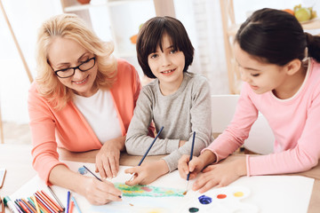 Beautiful elderly woman teaches children to draw. Little children draw. Drawing lessons.