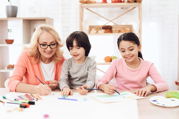 Beautiful egrandmother teaches grandchildren to draw. Children draw with paints.