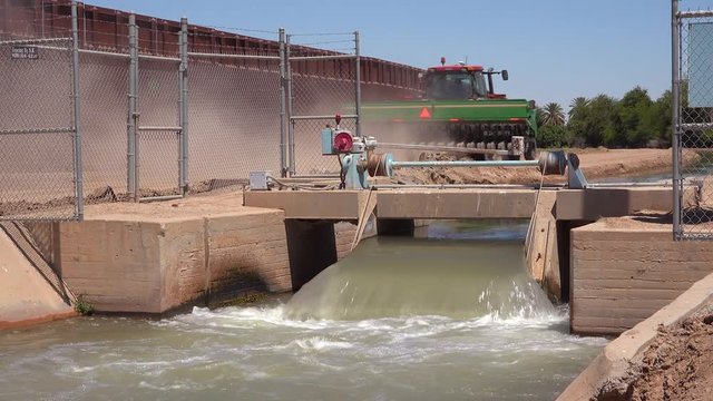 A farmers tractor follows a tributary of the Colorado River as it flows along the border wall between the US and Mexico.