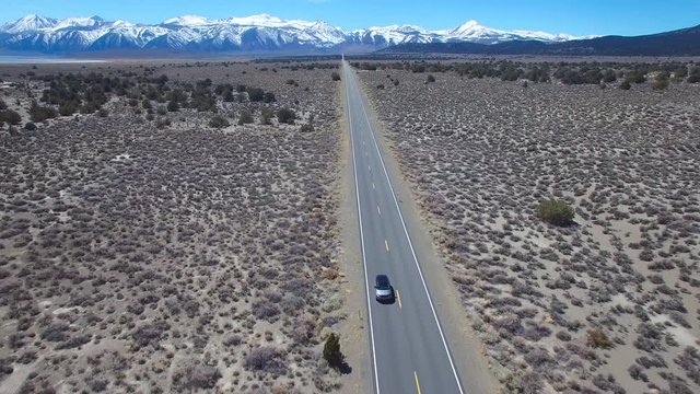 Aerial above a 4WD traveling on a paved road in the Mojave Desert with the Sierra Nevada mountains distant.