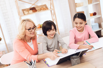 Grandmother helps to make lessons for grandchildren. Beautiful granny helps children learn.