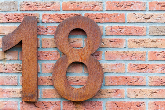 Rusted number eighteen in red on a brick wall