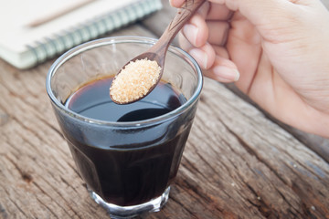 Glass of black coffee with woman hand put a spoon of brown sugar, Diet fitness and Unhealthy concept