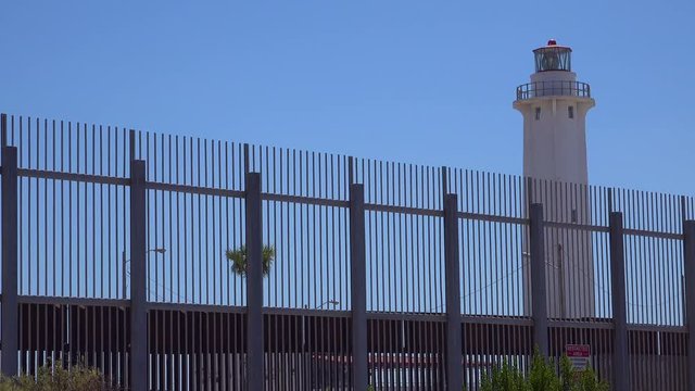 Establishing shot of the Tijuana border wall fence and lighthouse distant.