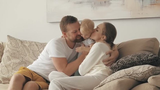 Happy parents embracing and kissing little daughter sitting on couch
