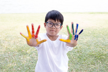 Asian boy in white t-shirt with colorful paint on his fingers with garden scene