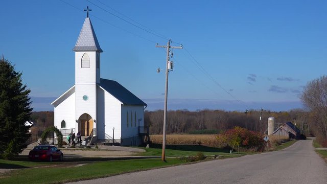 Churchgoers arrive at a pretty white church in the countryside.